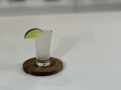 a small glass with a lime slice on the rim sits on a wooden coaster, ready to be used as a drink