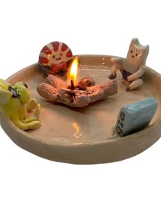 small ceramic figurines sitting on a plate with a lit candle in the middle