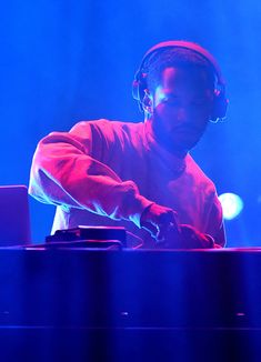 a man with headphones on playing music at a concert in front of bright blue lights