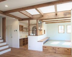 an empty room with wood flooring and white walls in the center, along with wooden steps leading up to a kitchen area