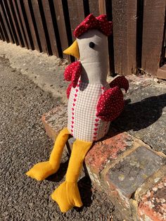 a stuffed chicken sitting on the ground next to a brick wall with a fence in the background