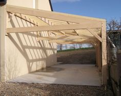 an unfinished wooden structure sitting in the middle of a gravel covered area next to a building