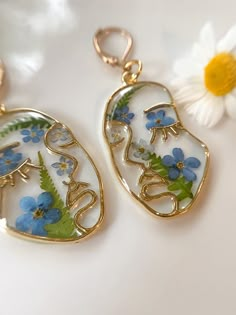 two gold tone earrings with blue flowers on them and the word love is written in white letters