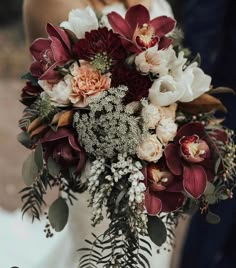 a bride holding a bouquet of red and white flowers with greenery in her hand