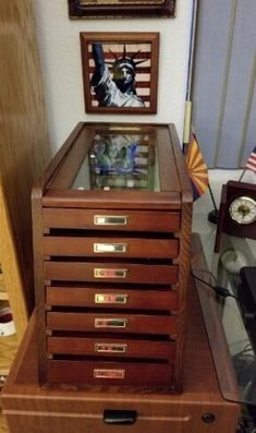 there is a wooden drawer with pictures on the wall behind it and an american flag