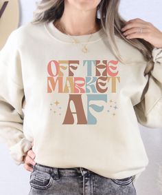 a woman wearing a sweatshirt with the words off the market af in multicolored letters