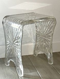 an acrylic glass table sitting on top of a hard wood floor next to a white wall