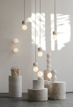 three white vases sitting next to each other on top of a cement floor with lights hanging from them