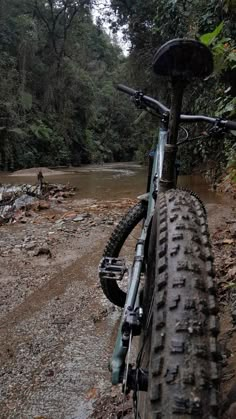 a mountain bike parked on the side of a muddy road next to a forest filled with trees