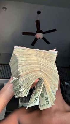 a person holding money in front of a ceiling fan