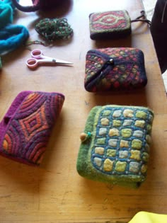 four small purses sitting on top of a wooden table next to scissors and yarn