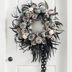 a wreath hanging on the front door with flowers and feathers attached to it's side