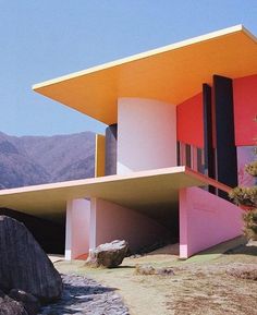 a pink and yellow building sitting on top of a hill next to a large rock