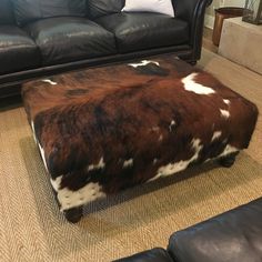 a cow hide ottoman sitting on top of a rug in front of a black couch