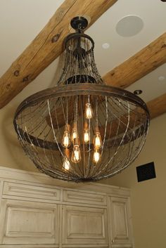 a chandelier hanging from the ceiling in a room with wood beams and white cabinets