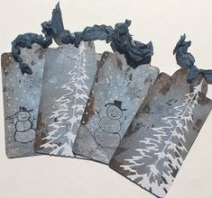 four tags with snowmen and pine trees on them are hanging from the side of a wall