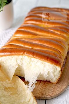 a loaf of bread with icing sitting on top of a wooden cutting board next to a potted plant