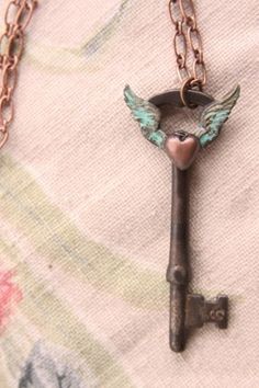 an antique key with angel wings attached to it is sitting on a floral fabric background