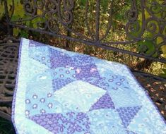 an iron bench with a blue quilt on it's seat and green leaves in the background