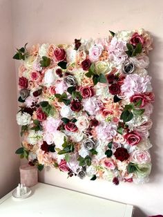 a white dresser topped with a vase filled with pink and red flowers next to a wall mounted flower art piece