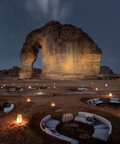 an outdoor seating area in front of a rock formation with candles lit up around it