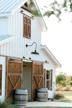 a barn with two wooden barrels in front of it and a light on the side