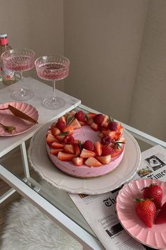 there is a cake with strawberries on the plate and two glasses next to it