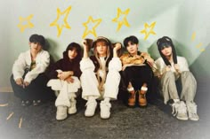 four young people sitting on the floor with their hands up in front of them and stars painted on the wall behind them