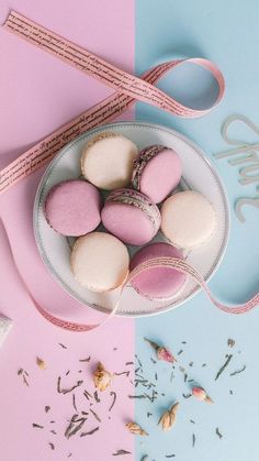 pink and white macaroons are in a bowl next to a measuring tape on a blue and pink background