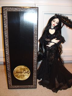 a doll in a black dress next to a box