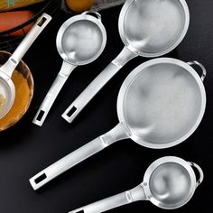 four stainless steel kitchen utensils with strainers and graters on a black surface