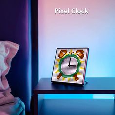 a small clock sitting on top of a table next to a pillow and blanket with the word pixel clock