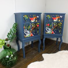 two blue nightstands with colorful designs on them next to a green potted plant