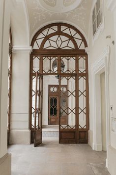 an arched wooden door in the middle of a hallway with white walls and flooring