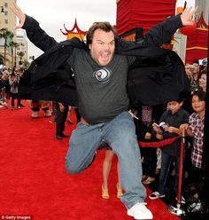 a man jumping in the air on a red carpet with his arms spread wide open