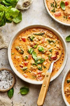 three bowls of soup with basil, tomatoes and other toppings on the table next to garlic