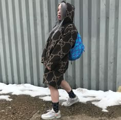 a woman with grey hair is walking in front of a metal wall wearing a hoodie and sneakers