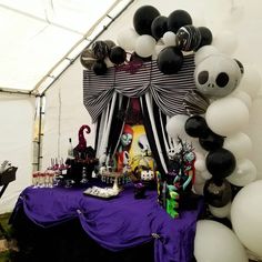 a table topped with balloons and decorations in front of a white tented area filled with black and white balloons