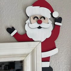 a wooden santa clause hanging on the wall next to a mirror with his arms in the air