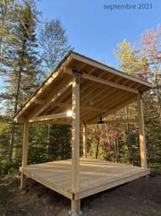 a wooden gazebo in the middle of a wooded area with trees and blue sky