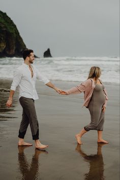 a man and woman holding hands while walking on the beach