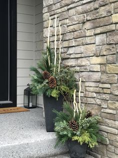 two planters filled with pine cones and evergreen needles on the steps to a house