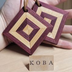 two handmade wooden coasters with the word koba written on them, in front of a person's hand