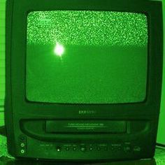 an old television sitting on top of a table in front of a green wall with the tv lit up