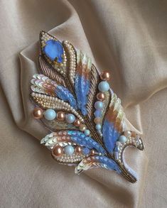 a blue and gold brooch sitting on top of a white cloth covered in pearls