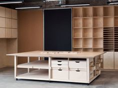 a large wooden table with drawers and shelves in an empty room, surrounded by cabinets