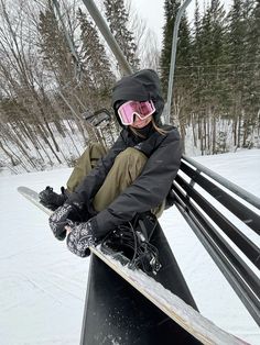 a person sitting on a ski lift with their snowboard in hand and wearing goggles