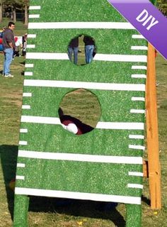 a large green and white board with holes in the grass next to people standing around