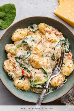 a bowl filled with pasta and spinach covered in cheese sauce next to two slices of cheese