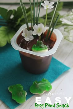 a potted plant with fake flowers in it on a blue towel next to some green frog candies